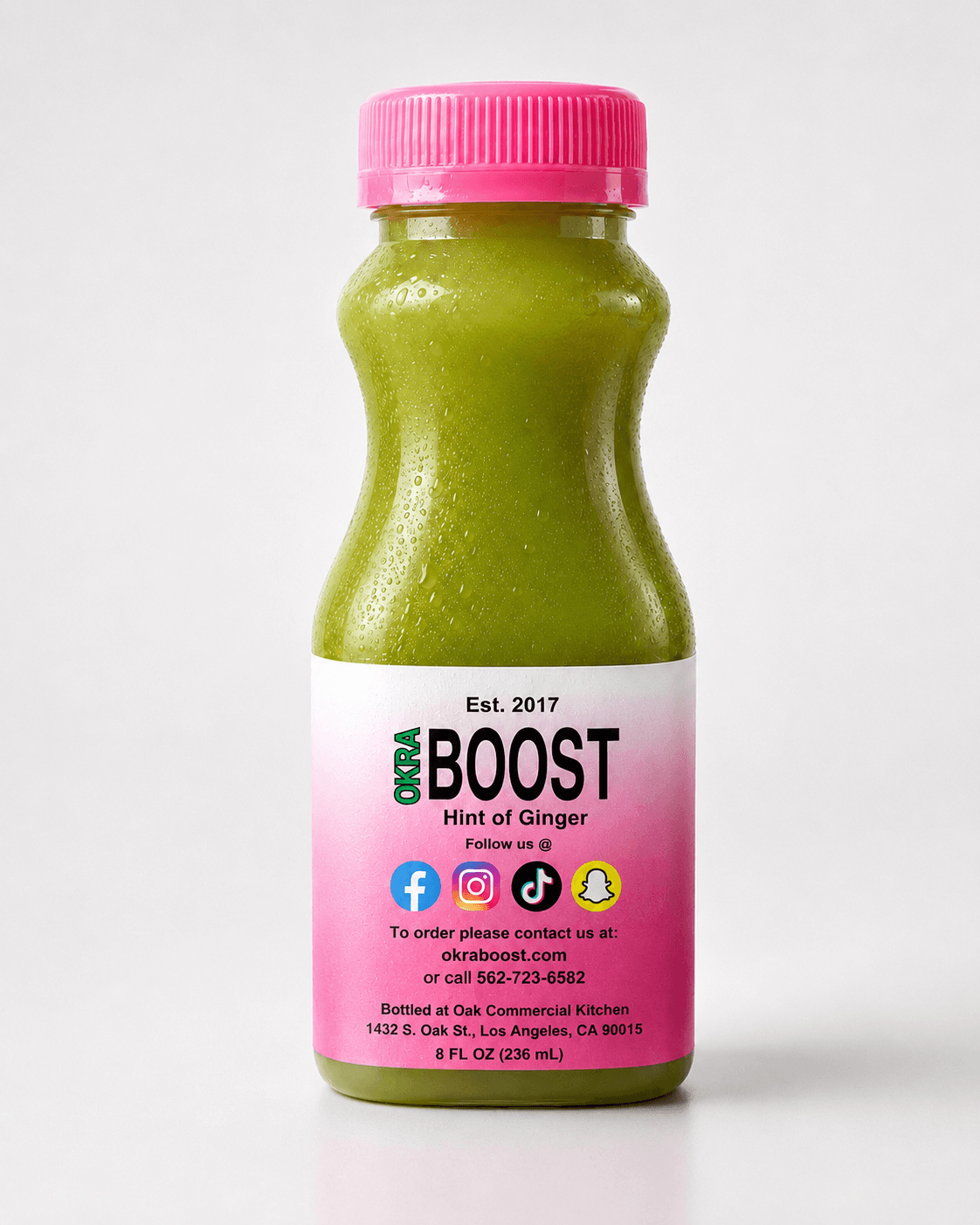 Okra Boost Ginger — pink-cap bottle with green-gold liquid, clean white studio backdrop